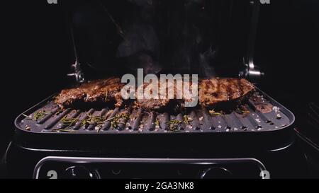 Deliziosa bistecca di carne succulenta cucinata alla griglia. Primi frittura di manzo su tostiera elettrica, rosmarino, pepe nero, sale. Movimento lento. Foto Stock