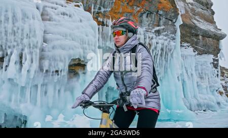 Donna è in bicicletta vicino alla grotta di ghiaccio. La roccia con ghiaccio c Foto Stock