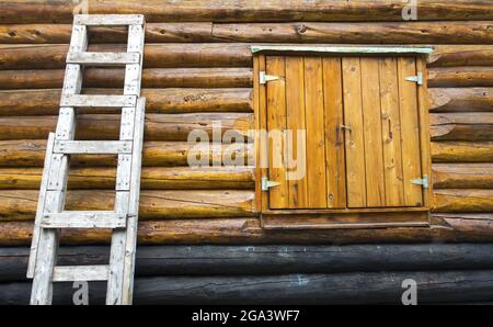 Vista frontale della cabina in legno rustico d'epoca con finestra chiusa e scala in legno sulla parete esterna in tessuto Foto Stock