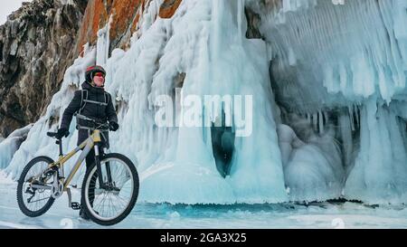 L'uomo sta pedalando vicino alla grotta di ghiaccio. Roccia con grotte di ghiaccio icicll Foto Stock