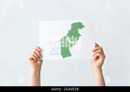 Mano femminile che tiene foglio di carta con la mappa della bandiera del Pakistan su sfondo chiaro Foto Stock