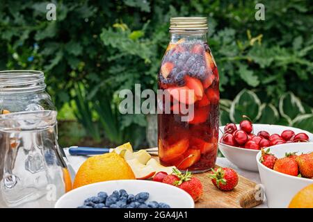 Punch fatto da frutti biologici e bacche. Rinfrescante bevanda estiva senza alcool con ghiaccio e succo di frutta. Bevanda fatta in casa in una bottiglia di vetro. Mele, s Foto Stock