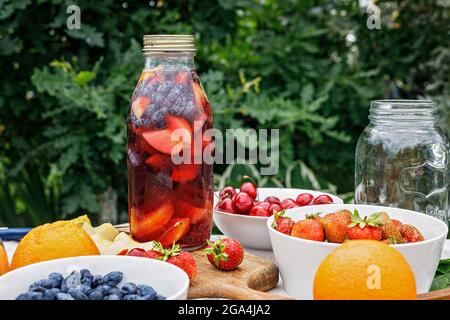 Rinfrescante sangria fredda o limonata fatta in casa con agrumi e bacche biologiche. Cocktail estivo con succo di frutta in bottiglia di vetro. Mele, paglia Foto Stock