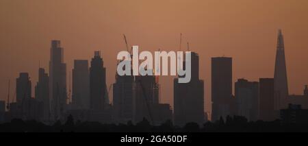 Wimbledon, Londra, Regno Unito. 29 luglio 2021. Un'alba limpida e fresca sullo skyline di Londra dopo un giorno precedente di pioggia torrenziale. Il sole che sorge illumina le facce orientali dei grattacieli in costruzione vicino a Battersea sul lato sud del fiume Tamigi e nasconde gradualmente le vedute degli edifici degli uffici della City of London. Credit: Malcolm Park/Alamy Live News. Foto Stock