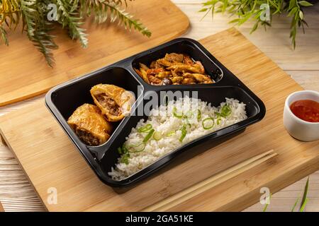 Riso con rotolo di maiale e stufato di pollo in scatola da take-out su tagliere di bambù Foto Stock