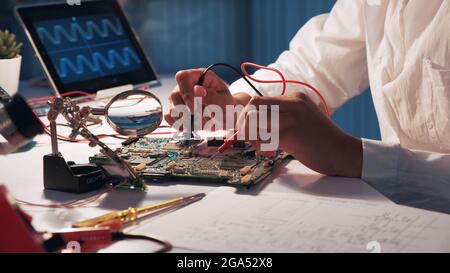 Vista delle mani delle donne che testano la scheda elettronica in laboratorio utilizzando un tester multimetro e altre tecnologie Foto Stock