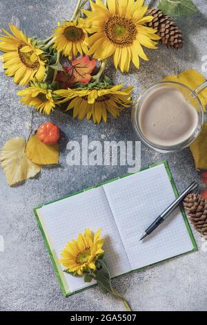 Buongiorno. Concetto di elenco attività. Un bouquet di grandi girasoli, una tazza di caffè e un taccuino vuoto su un tavolo di pietra. Vista dall'alto sfondo piatto. Foto Stock