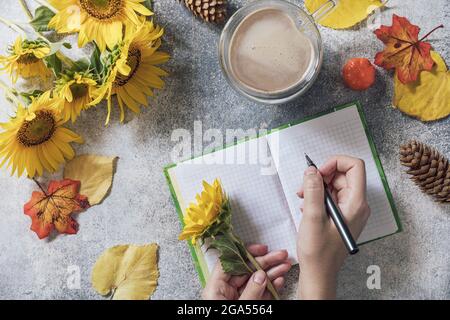 Buongiorno. Concetto di elenco attività. Un bouquet di grandi girasoli, una tazza di caffè e un taccuino vuoto su un tavolo di pietra. Vista dall'alto sfondo piatto. Foto Stock