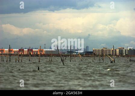 Una vista dall'acqua costiera di Bekasi appena prima del confine con Giacarta, Indonesia. La nuova area commerciale chiamata Marunda Makmur sull'estuario del canale alluvionale di Giacarta (a sinistra) e i nuovi edifici pianeggianti nel villaggio Marunda di Giacarta (a destra) sono fotografati sullo sfondo di alcuni degli edifici torreggianti della capitale. Foto Stock