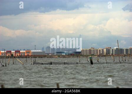 Una vista dall'acqua costiera di Bekasi appena prima del confine con Giacarta, Indonesia. La nuova area commerciale chiamata Marunda Makmur sull'estuario del canale alluvionale di Giacarta (a sinistra) e i nuovi edifici pianeggianti nel villaggio Marunda di Giacarta (a destra) sono fotografati sullo sfondo di alcuni degli edifici torreggianti della capitale. Foto Stock