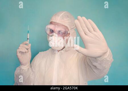 Ritratto del medico maschile in indumenti protettivi, guanti e maschera che tengono una siringa e mostrando un gesto proibitivo con le mani. Medicina e assistenza sanitaria co Foto Stock