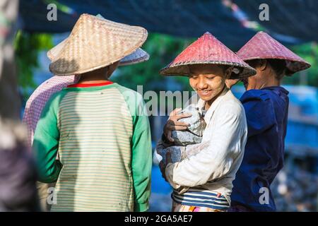 Lavoratrice manuale femminile che indossa cappello conico porta grandi rocce nelle sue braccia, Mandalay, Myanmar (Birmania) Foto Stock