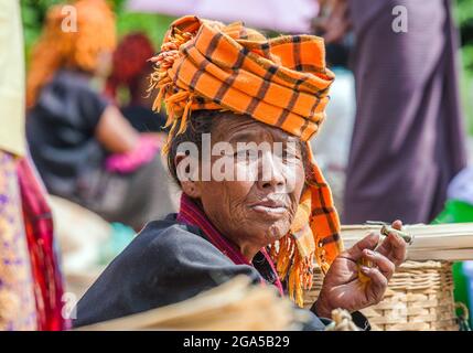 Commerciante di mercato da Pa'o (Pa-o) tribù di collina che indossa turbano arancione sigaro che fuma la vendita di verdure a Kalaw, Stato di Shan, Myanmar Foto Stock