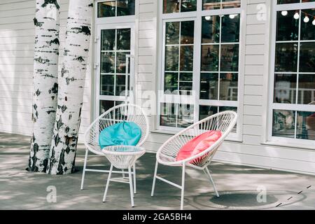 Tavoli bianchi vuoti all'esterno della caffetteria del ristorante. Sedia con cuscini colorati sul marciapiede all'aperto. Nessuno Foto Stock