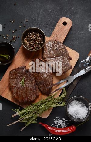 Succulenta bistecca di manzo alla griglia con rosmarino, carne fritta, primo piano. Bistecche Top Blade su tavola di legno Foto Stock