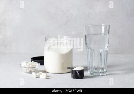 Polvere di collagene in vaso e misurino, capsule di collagene e un bicchiere d'acqua su sfondo grigio. Concetto sano e antiage Foto Stock