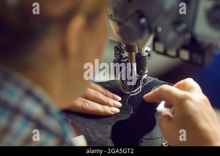 Calzaturiera che fa un dettaglio per nuove calzature su una macchina da cucire industriale Foto Stock