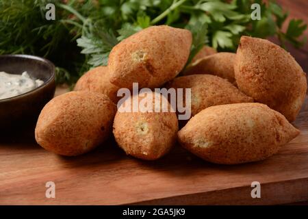 Kibbeh di carne macinata fritta mescolata al bulgur, farcito con carne tritata fritta con pinoli su un piatto di argilla su tavola di legno Foto Stock