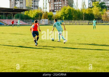 Giocatori di calcio in azione nello stadio, gioco di calcio per adulti, giocatori di due squadre che gareggiano per la palla, giocatori di calcio che saltano in alto sul Foto Stock