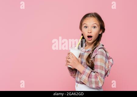 Stupito bambino che tiene il milkshake con la paglia bevente isolata su rosa Foto Stock