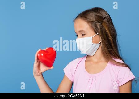 Capretto presteen in maschera medica guardando il cuore rosso isolato su blu Foto Stock