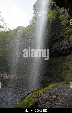 Fotografia scattata guardando fuori da dietro le cascate di Henrhyd, Neath, la cascata più alta del Galles meridionale, a 90 metri. Foto Stock