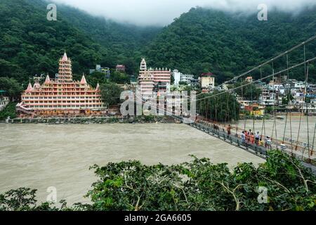 Rishikesh, India - 2021 luglio: Persone che passano dal ponte Lakshman Jhula accanto al tempio Swang Niwas a Rishikesh il 20 luglio 2021 a Uttarakhand, Foto Stock