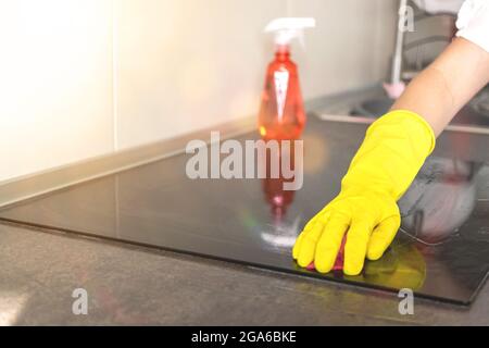 Donna che pulisce stufa elettrica con panno per stoviglie e bottiglia spray su fondo cucina Foto Stock