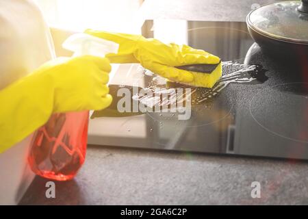 Mano in guanto di gomma gialla lava una stufa elettrica in una giornata di sole, fondo di concetto di pulizia della cucina Foto Stock