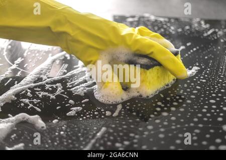 Mano in guanto di gomma gialla lava una stufa elettrica in cucina, concetto di pulizia della cucina, primo piano vista foto Foto Stock