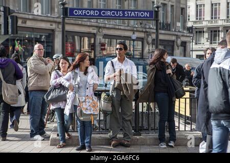 Londra, Regno Unito - 2019 novembre, la gente attraversa la strada all'ora di punta su Oxford Street, la strada principale dello shopping. Uomo e donna in attesa di amici vicino tubo Foto Stock