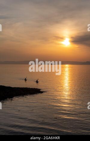 kayak al tramonto due canoisti che si addormentano al crepuscolo al tramonto sulla costa dell'ayrshire in scozia Foto Stock