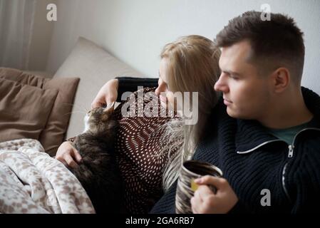 Giovane famiglia con gatto domestico e tazza da tè sul divano a casa Foto Stock