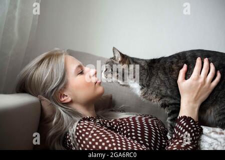 Giovane donna graziosa con gatto domestico cute sta posando sul divano a casa Foto Stock