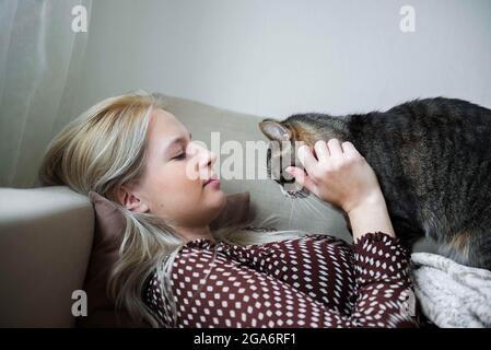 Giovane donna graziosa con gatto domestico cute sta posando sul divano a casa Foto Stock