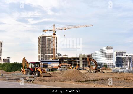 Grande cantiere con gru a torre in azione e attrezzature per il movimento terra. Costruzione di nuovi edifici residenziali a più piani e business cen Foto Stock