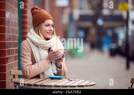 Donna che siede all'esterno della caffetteria sulla Busy City High Street in autunno Foto Stock