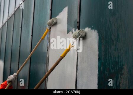 Dipinge i graffiti con un rullo. Il molare dipinge la parete con vernice bianca. Uno strumento per la verniciatura rapida delle superfici. Foto Stock