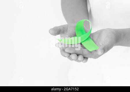 Mani che tengono il nastro verde smeraldo o verde giada su sfondo bianco  del tessuto con spazio di copia, simbolo per la consapevolezza del cancro  del fegato, Giornata Mondiale del cancro. Guarire Foto stock - Alamy