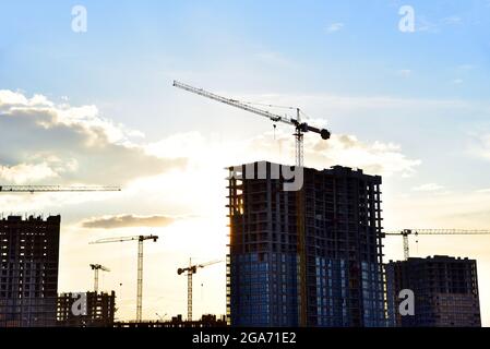 Gru a torre in azione su sfondo tramonto. Costruzione nuovo edificio residenziale su sfondo blu cielo. Lavoratori costruttori durante le casseforme e versamenti Foto Stock