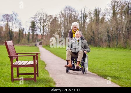Donna anziana che spinge l'uomo anziano in sedia a rotelle all'aperto in autunno o inverno Foto Stock