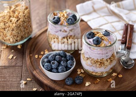 Parfait con mirtilli, muesli e yogurt in un bicchiere su un rustico tavolo di legno Foto Stock