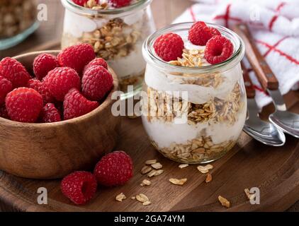 Parfait di granola con yogurt e lamponi freschi su un piatto di legno Foto Stock