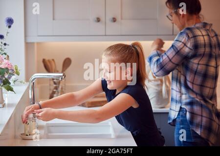 Madre con figlia lavando le mani con sapone a casa per fermare la diffusione di infezione in Pandemic di salute Foto Stock