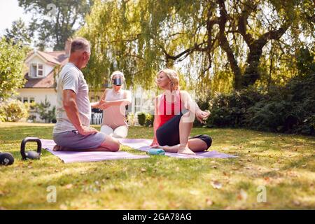 Coppia senior che partecipa a una lezione privata di yoga socialmente distanziata con insegnante a casa Foto Stock
