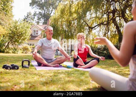 Coppia senior che partecipa alla lezione privata di yoga con insegnante in Giardino a casa Foto Stock