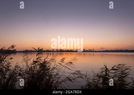 Tramonto sullo skyline di Rotterdam visto da Kralingse Plas (Lago Kralingen) con cielo colorato che si riflette nelle acque ferme del lago Foto Stock