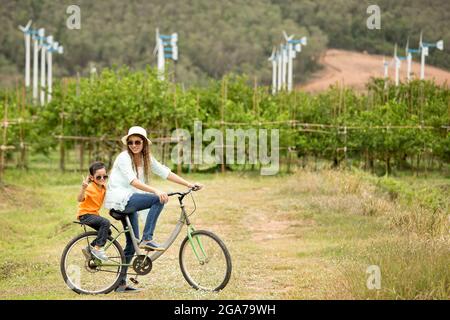 Donna e ragazzo in bicicletta in fattoria con turbine eoliche in background Foto Stock