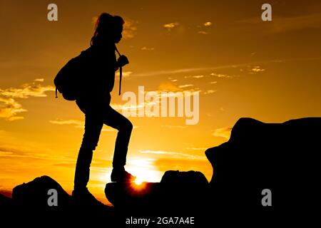 Donna che cammina sulla cima della montagna al crepuscolo con il raggio del sole sotto i suoi piedi Foto Stock