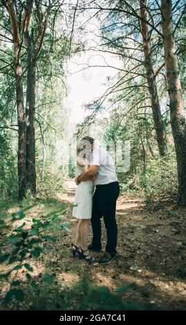 Giovane coppia alla moda nella foresta. Un ragazzo e una ragazza si abbracciano insieme sotto un grande albero vecchio su uno sfondo di una foresta. Faccia irriconoscibile Foto Stock